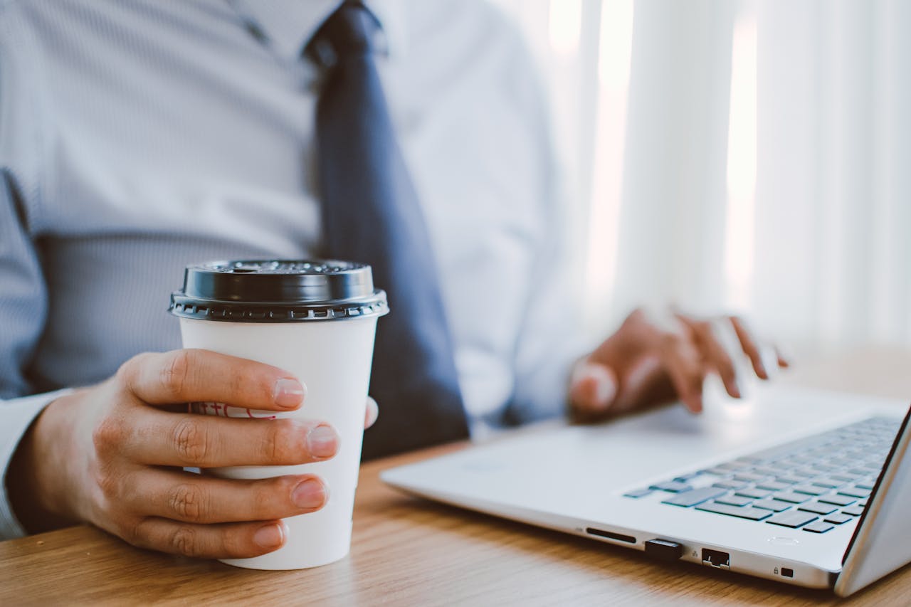 Business professional working remotely, enjoying coffee while using a laptop indoors.